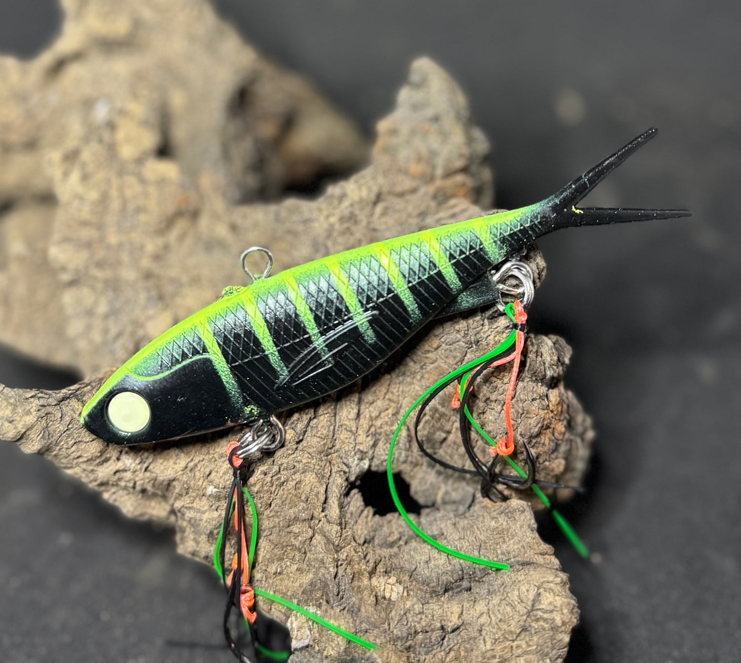 A multicoloured fishing lure with a vibrating tail designed to imitate the movement of fish, equipped with two sets of stinger hooks.