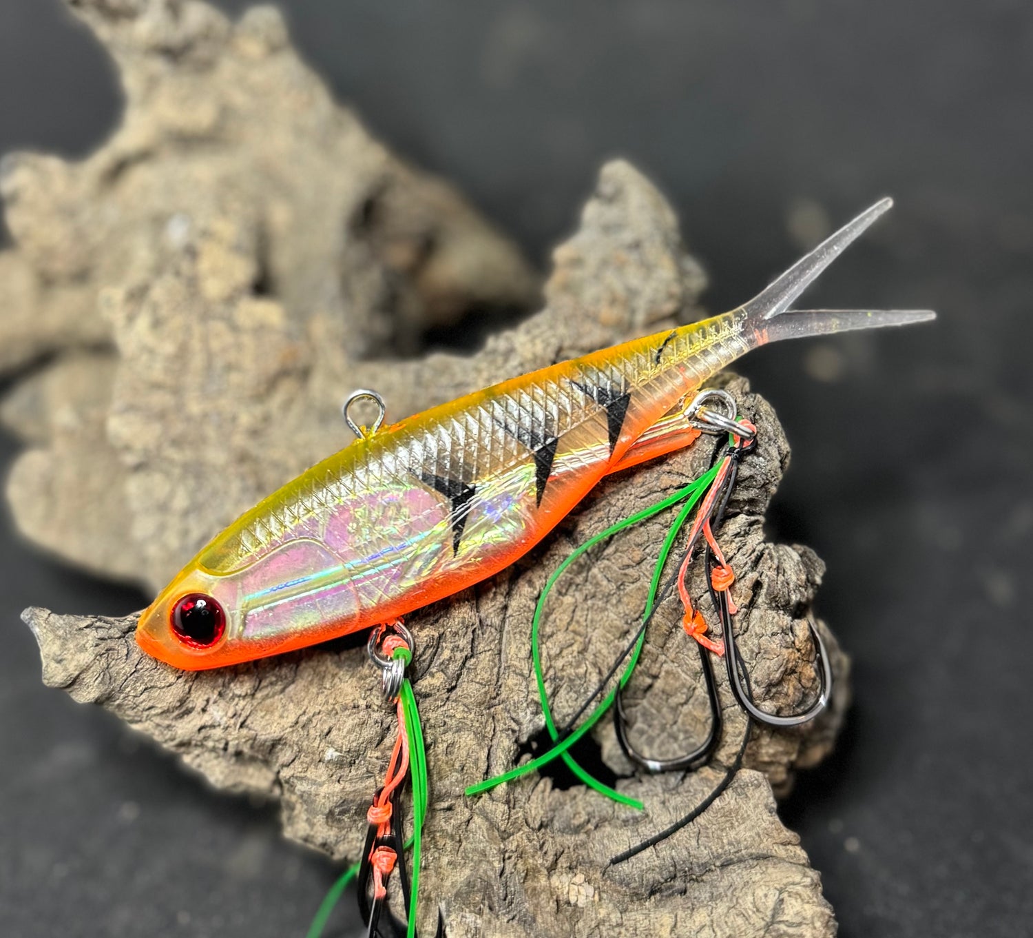 A multicoloured fishing lure with a vibrating tail designed to imitate the movement of fish, equipped with two sets of stinger hooks.