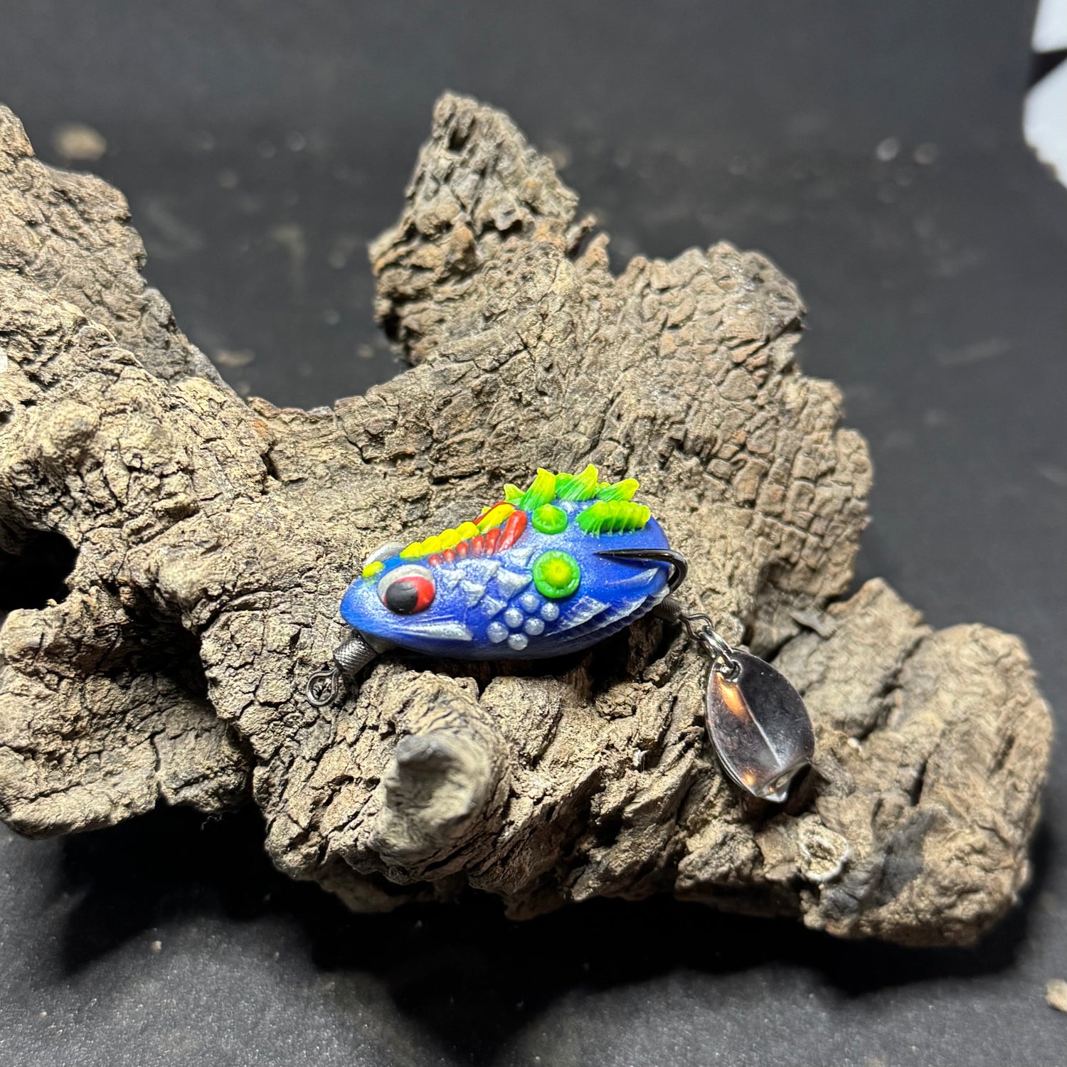 A collection of colorful fishing lures designed to resemble frogs, displayed on a piece of driftwood.