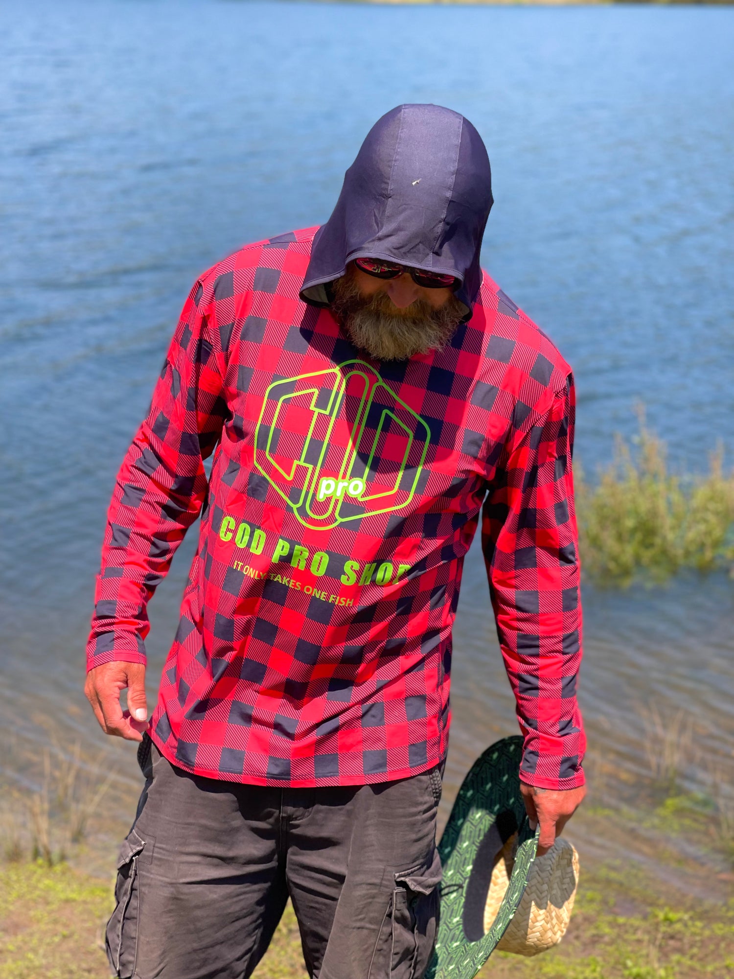 A person wearing a red and black checkered fishing shirt with a hood, featuring a graphic logo, cod pro shop