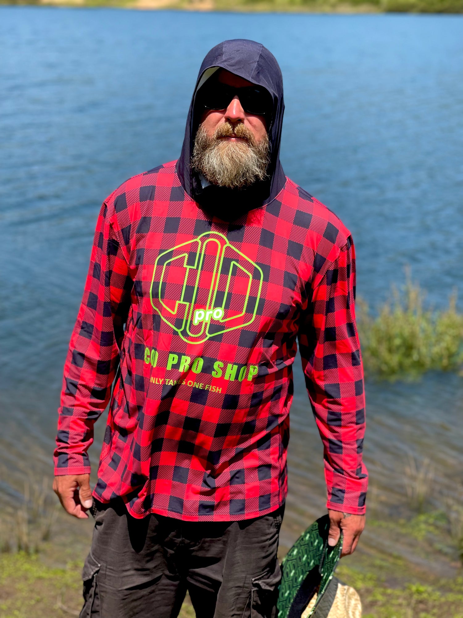 A person wearing a red and black checkered fishing shirt with a hood, featuring a graphic logo, cod pro shop