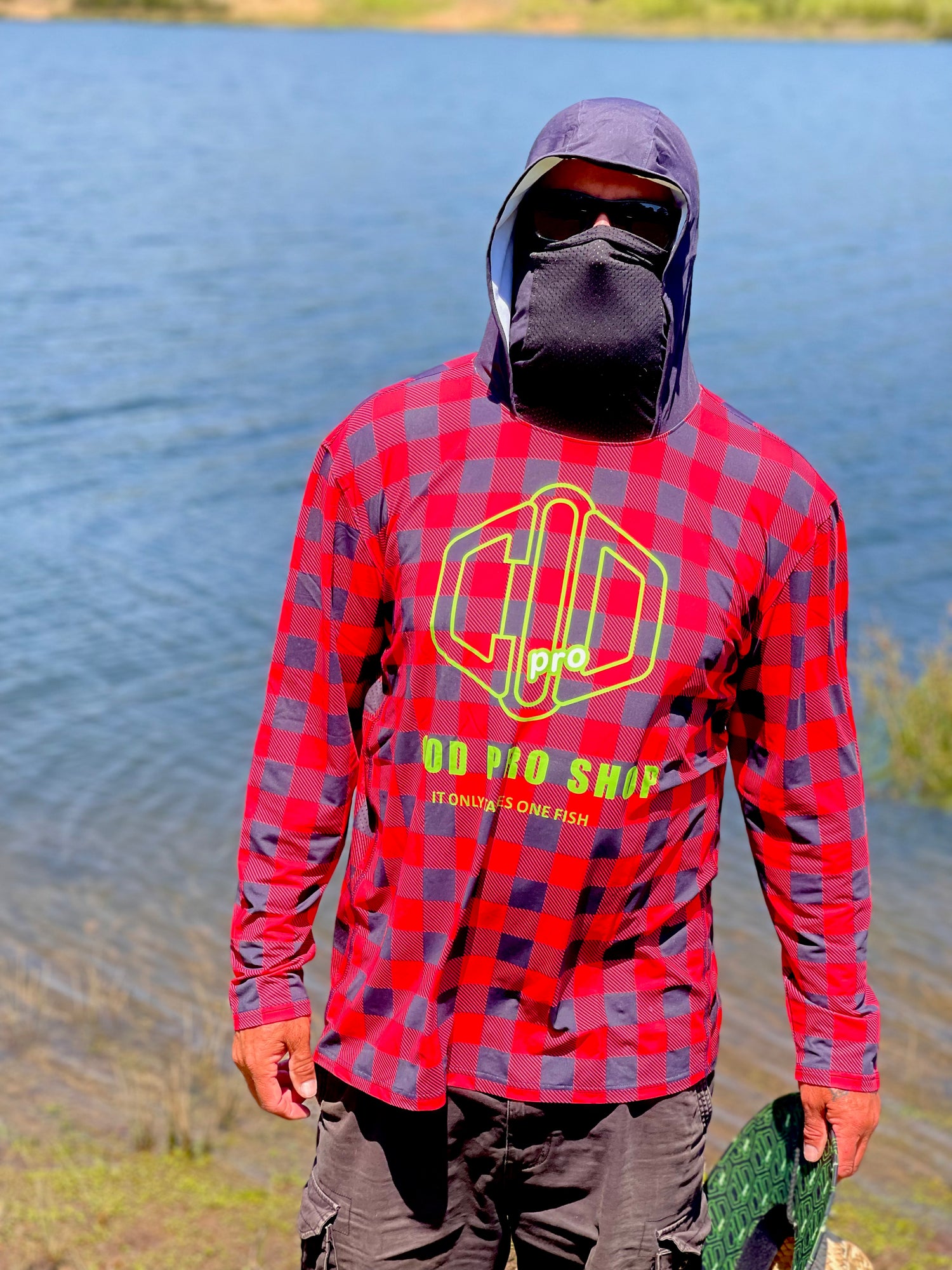 A person wearing a red and black checkered fishing shirt with a hood, featuring a graphic logo, cod pro shop