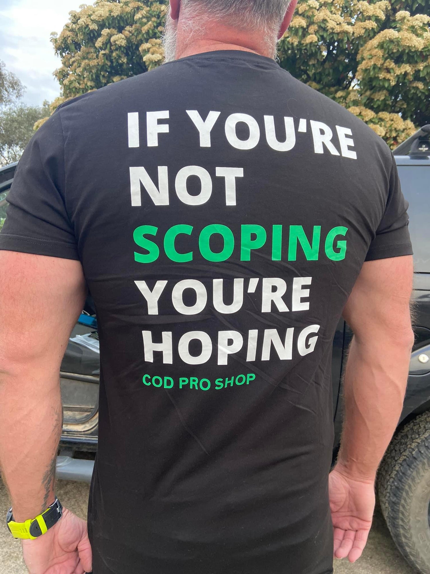 A man wearing a dad body t-shirt black short sleeve t-shirt with a subtle logo on the back,