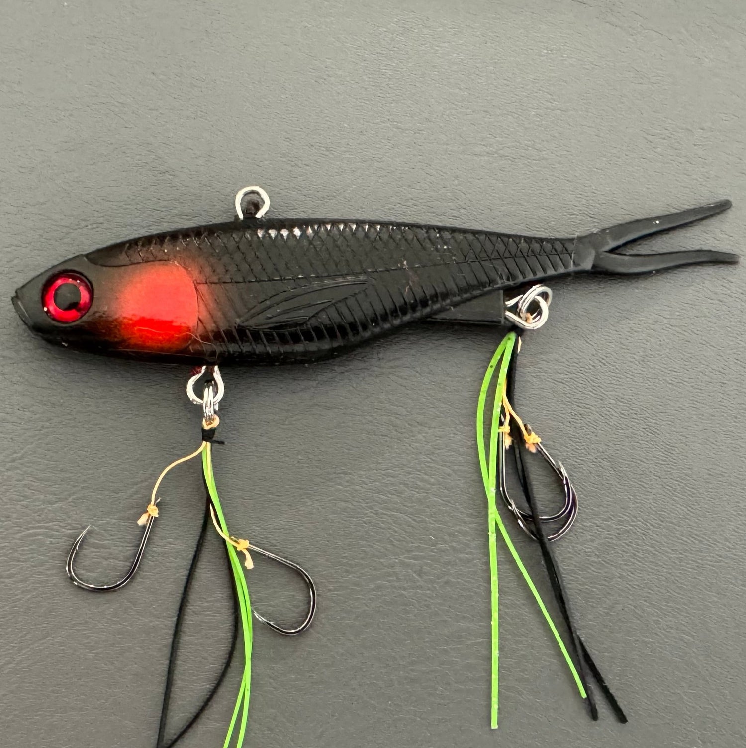 A multicoloured fishing lure with a vibrating tail designed to imitate the movement of fish, equipped with two sets of stinger hooks.