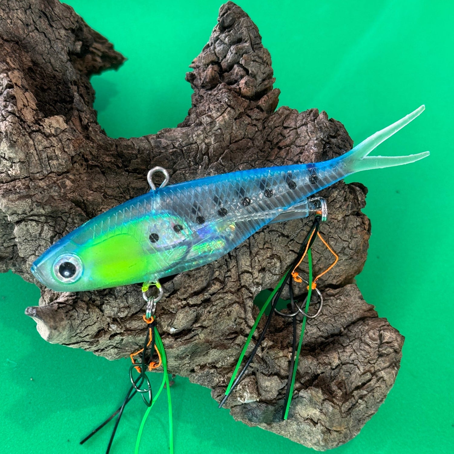 A multicoloured fishing lure with a vibrating tail designed to imitate the movement of fish, equipped with two sets of stinger hooks.