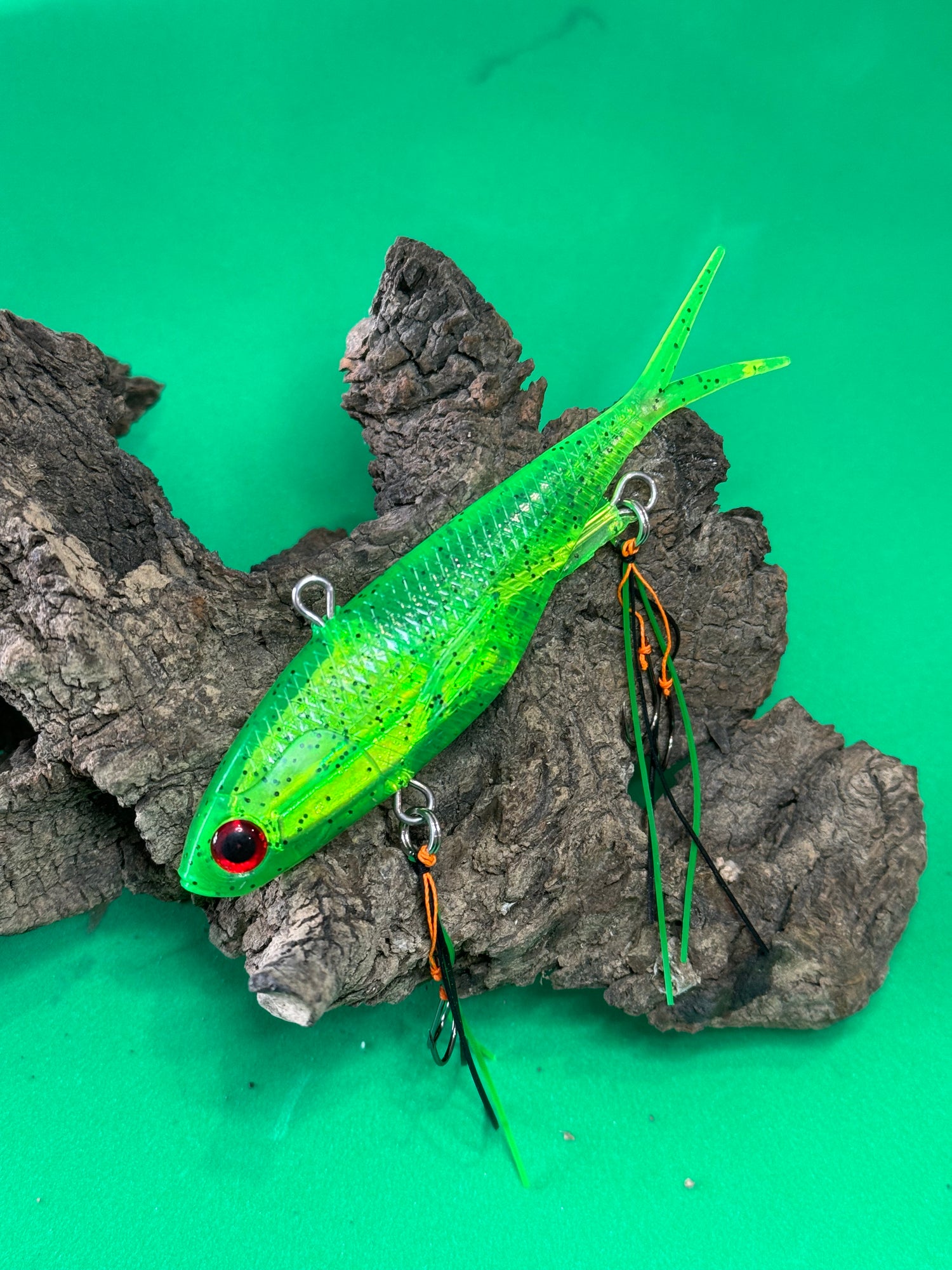 A multicoloured fishing lure with a vibrating tail designed to imitate the movement of fish, equipped with two sets of stinger hooks.