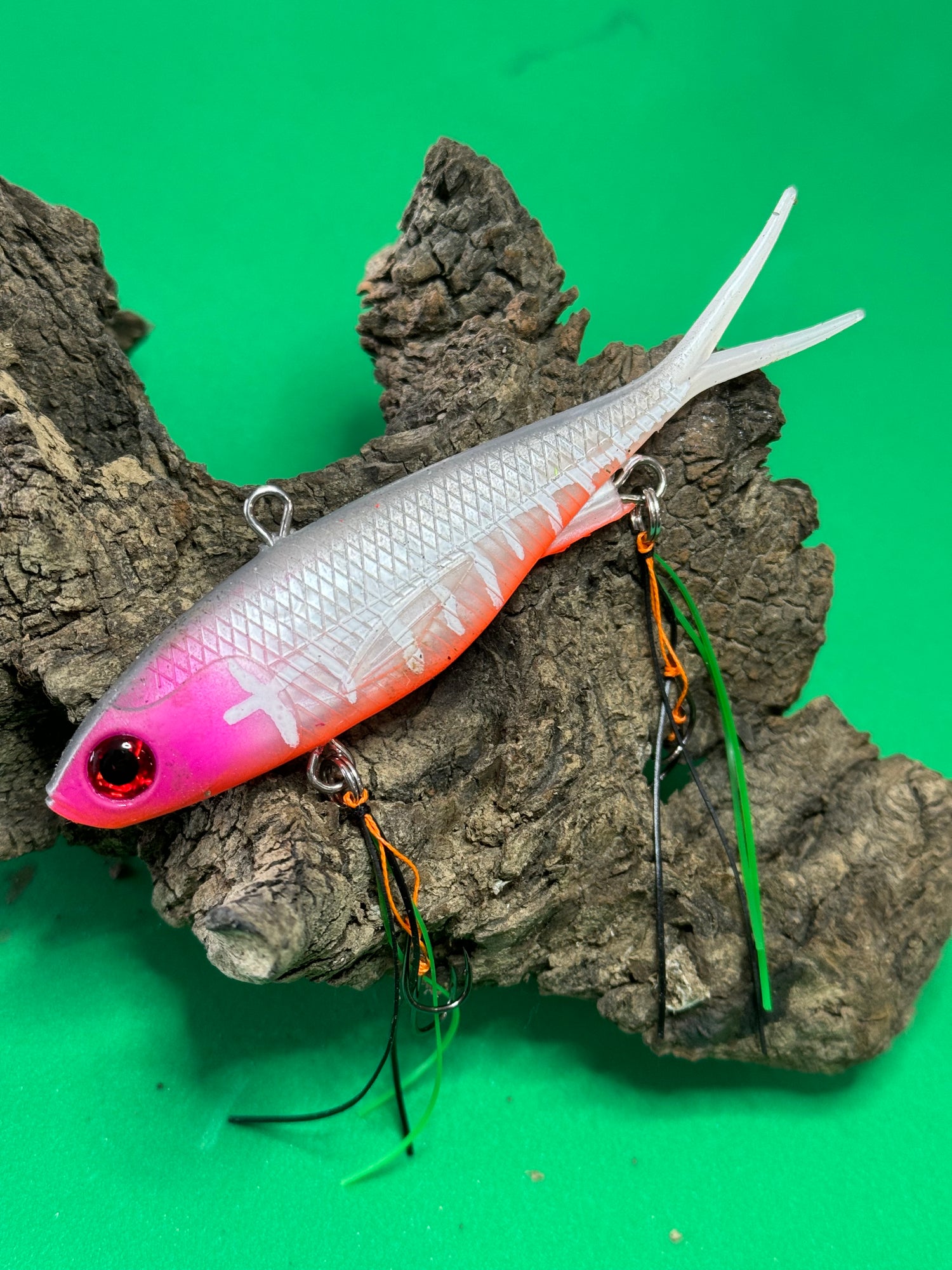 A multicoloured fishing lure with a vibrating tail designed to imitate the movement of fish, equipped with two sets of stinger hooks.