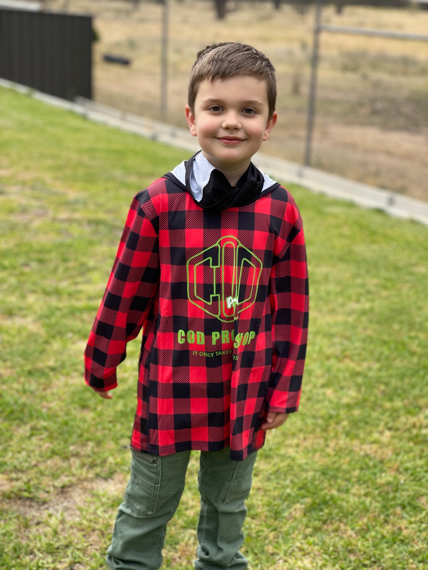 A child wearing a red and black checkered fishing shirt with long sleeves and a hood, standing outdoors.