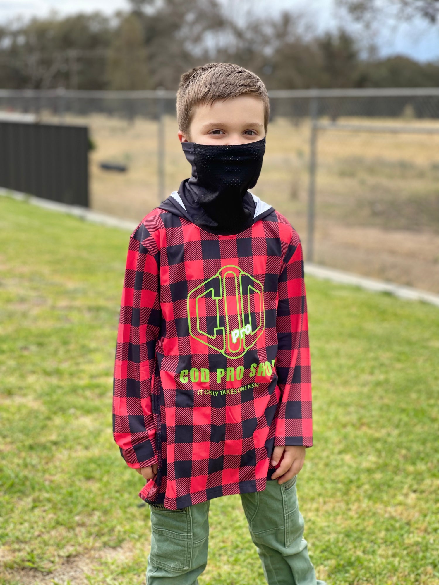 A child wearing a red and black checkered fishing shirt with long sleeves and a hood, standing outdoors.
