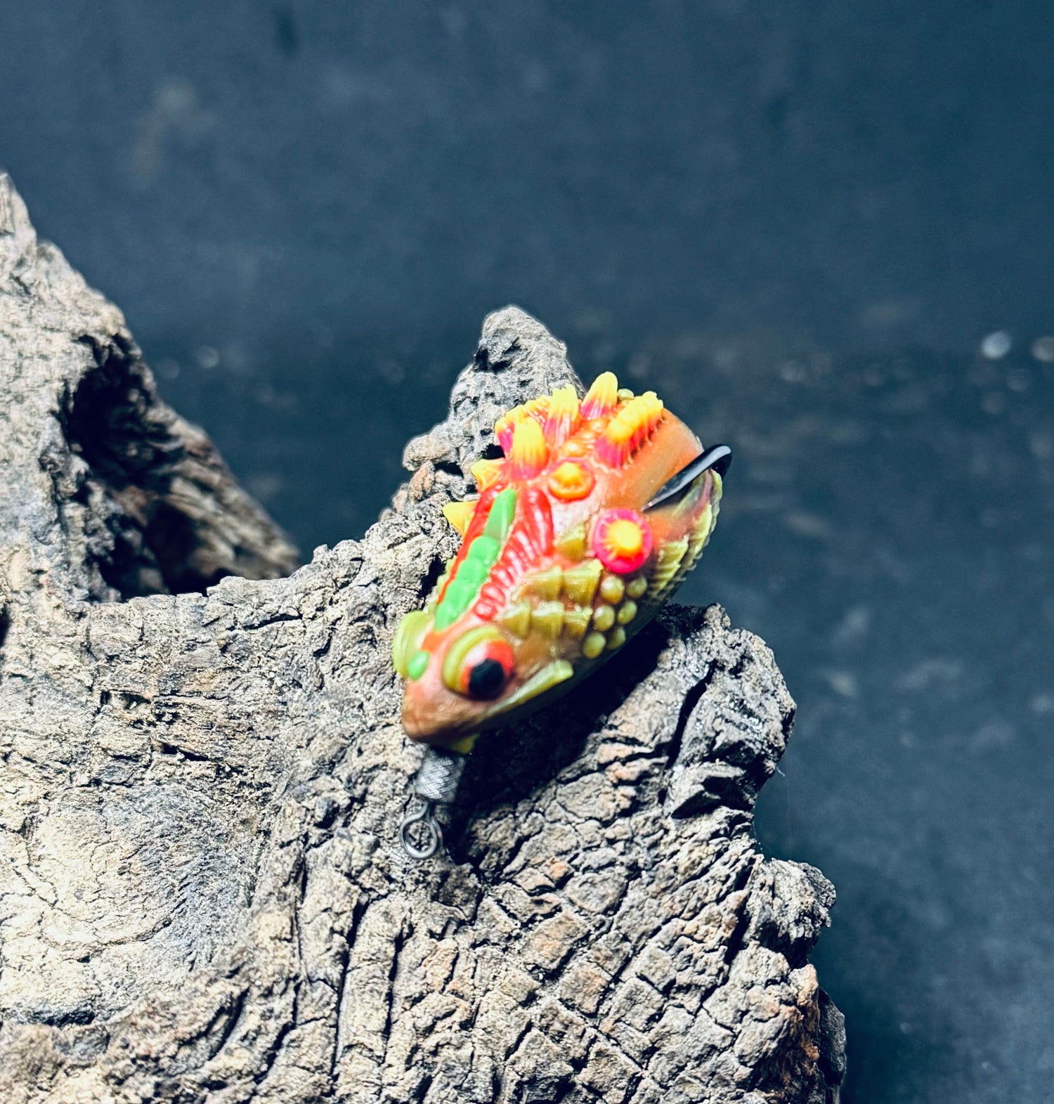A collection of colorful fishing lures designed to resemble frogs, displayed on a piece of driftwood.