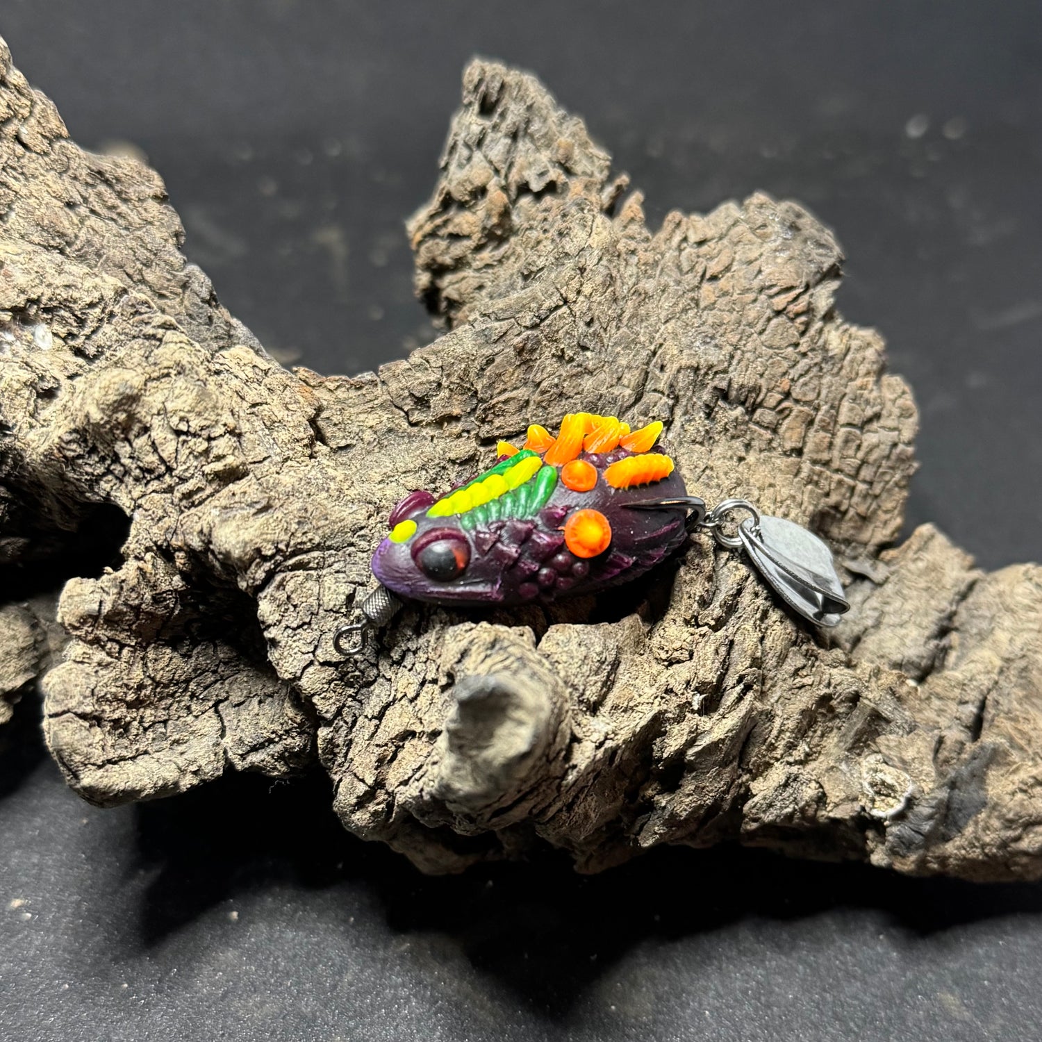 A collection of colorful fishing lures designed to resemble frogs, displayed on a piece of driftwood.