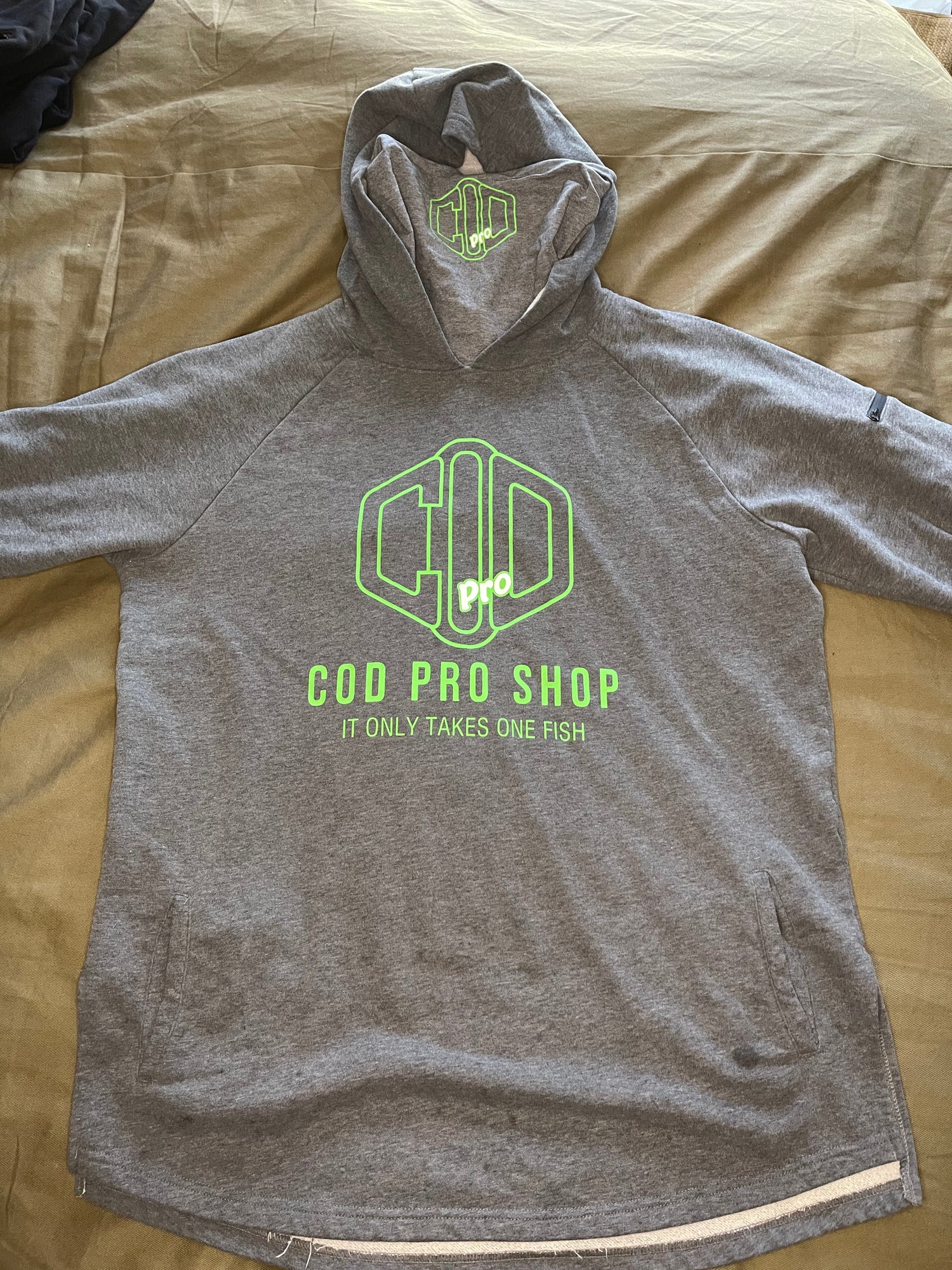 A grey hoodie with the text 'COD PRO SHOP' displayed prominently, featuring a hood and a built-in neck scarf. The hoodie is presented on a mannequin against a black background.