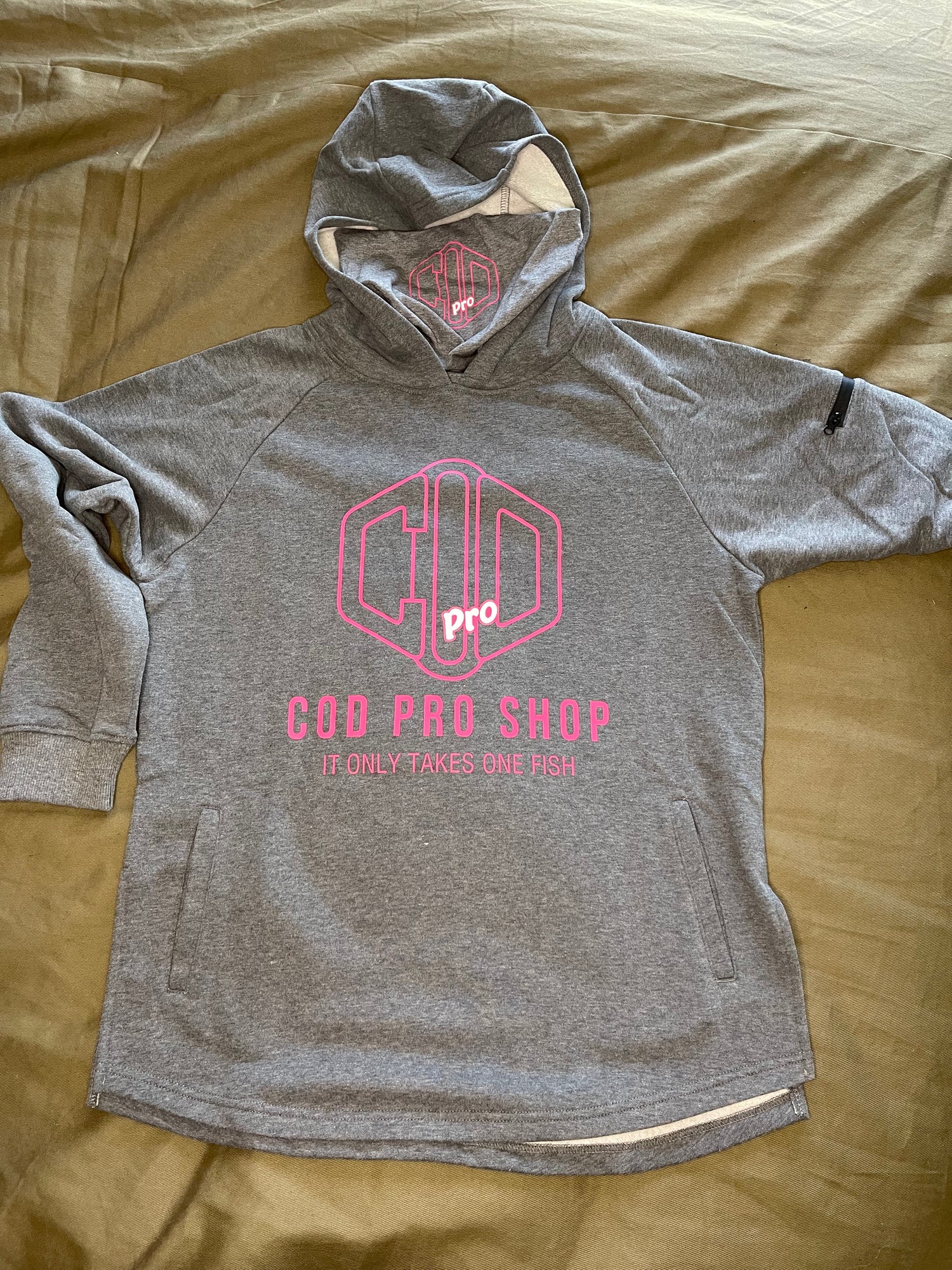 A grey hoodie with the text 'COD PRO SHOP' displayed prominently, featuring a hood and a built-in neck scarf. The hoodie is presented on a mannequin against a black background.