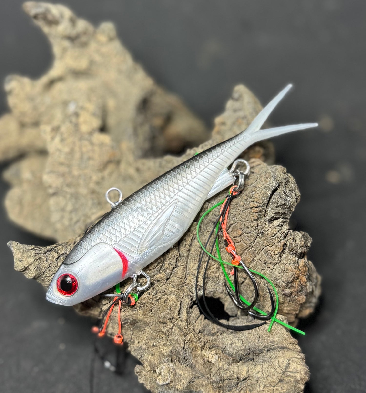 A multicoloured fishing lure with a vibrating tail designed to imitate the movement of fish, equipped with two sets of stinger hooks.