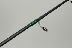 Close-up of a fishing rod handle with a green grip on a wooden floor.