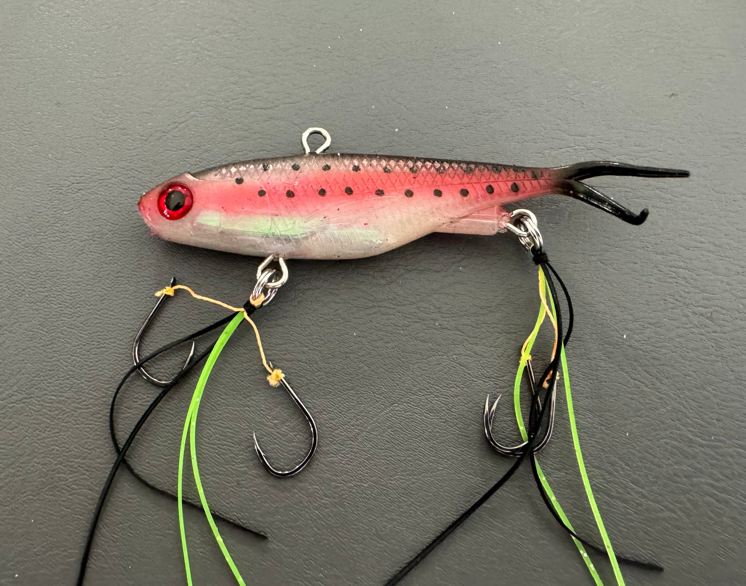 A multicoloured fishing lure with a vibrating tail designed to imitate the movement of fish, equipped with two sets of stinger hooks.